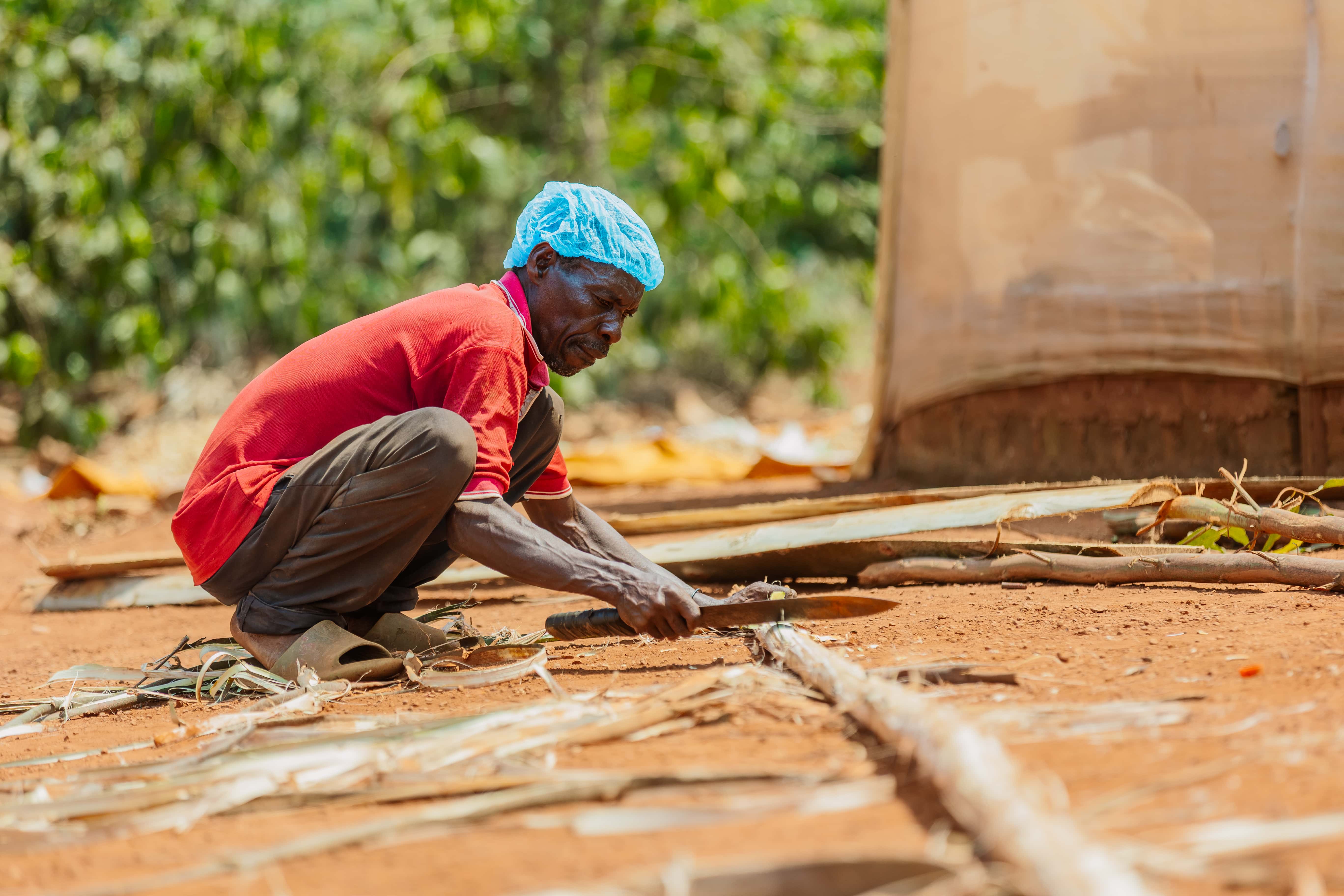 A community worker preparing natural materials beside the solar dryer